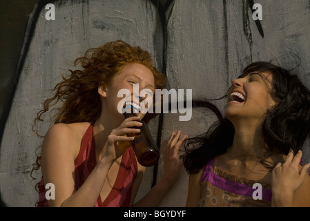 Deux jeunes femmes à l'extérieur, à rire, à un holding glass verre bouteille Banque D'Images