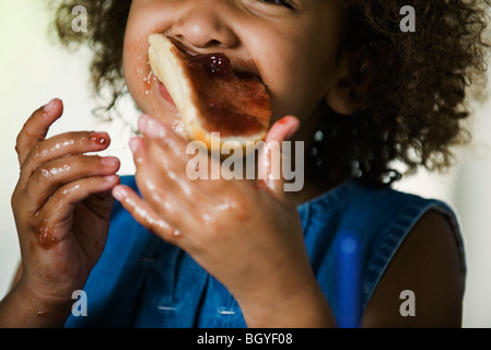 Little girl eating snack, les mains et le visage couvert de jam Banque D'Images