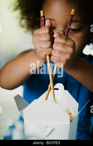 Petite fille du mal à manger les plats à emporter avec des baguettes Banque D'Images