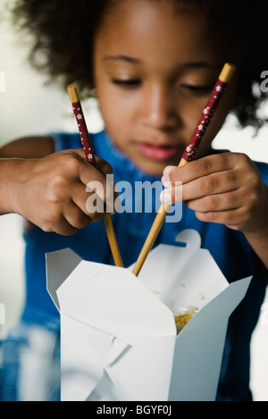 Petite fille de manger les plats à emporter avec des baguettes Banque D'Images