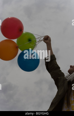 Femme holding bunch of balloons vers ciel nuageux Banque D'Images
