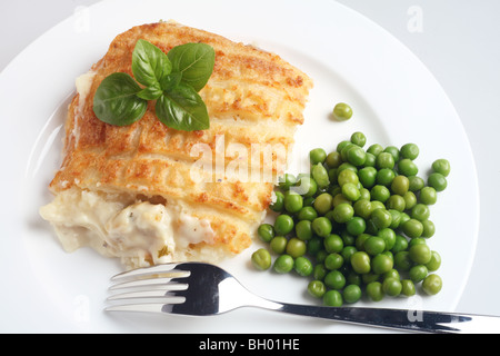 Un poisson classique les tartes faites de la purée de pommes de terre cuites sur le dessus de sauce béchamel et poissons cuits, avec des pois verts et garnir de basilic Banque D'Images