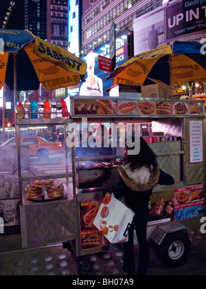 Une femme afro-américaine s'arrête pour un hot-dog à partir d'un panier de trottoir à New York'S Times Square avec ses affiches extérieures. Banque D'Images