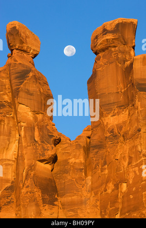 Près de la pleine lune avec les trois commères, Arches National Park, près de Moab, Utah. Banque D'Images