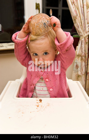 Close up portrait of vertical d'un bébé fille obtenant un gâchis de mettre son bol de glace au chocolat sur la tête. Banque D'Images
