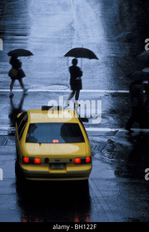 Piétons sous les rues bordeaux dans Crosswalk et taxi dans la pluie, New York Banque D'Images