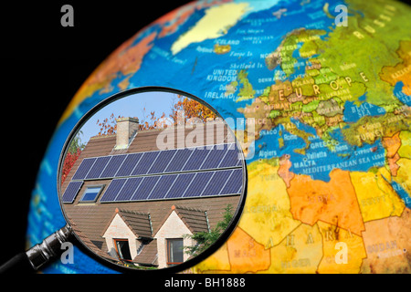 Panneaux solaires photovoltaïques sur le toit de cellules / maison vue à travers la loupe tenu contre allumé globe terrestre Banque D'Images