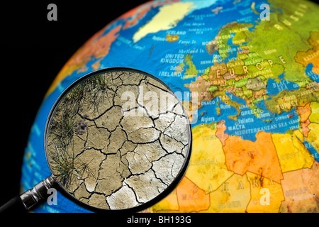 La terre craquelée par la sécheresse vu à travers une loupe tenu contre allumé globe terrestre Banque D'Images