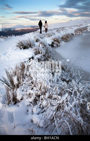 Couple en train de marcher dans la neige sur les maures aux côtés du gardien congelés Étang et mont du Pain de sucre dans la montagne Blorenge distance Wales UK Banque D'Images