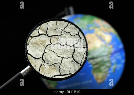 La terre craquelée par la sécheresse vu à travers une loupe tenu contre allumé globe terrestre Banque D'Images