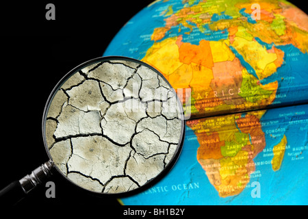 La terre craquelée par la sécheresse vu à travers une loupe tenu contre allumé globe terrestre Banque D'Images