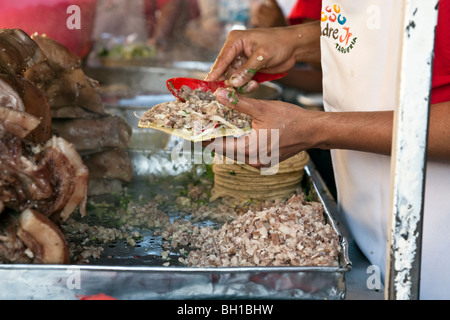 Mains d'un homme de décisions à un tacos de porc avec un étal de taco en cours & ingrédients ci-dessous sur des plateaux dans la ville d'Oaxaca au Mexique Banque D'Images