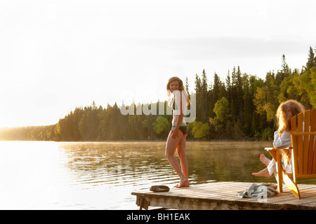 Femme debout en maillot, deuxième femme assise dans une chaise sur dock, Clear Lake, Manitoba, Canada