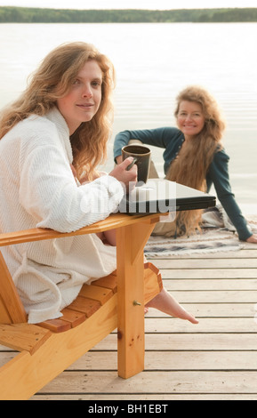 Woman in deck chair smiling at camera, deuxième femme assise sur un quai, Clear Lake, Manitoba, Canada Banque D'Images