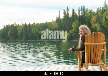 Rivage d'arbres avec femme assise dans une chaise sur dock, Clear Lake, Manitoba, Canada Banque D'Images