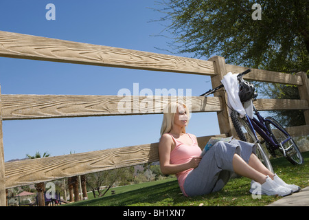 Jeune femme assise leaning against fence Banque D'Images