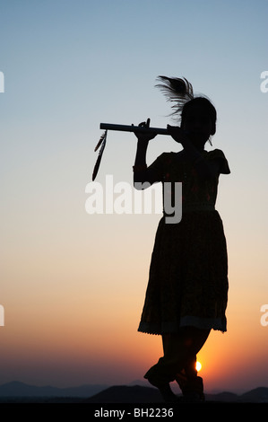 Silhouette d'une jeune indienne se faisant passer pour le Seigneur krishna au coucher du soleil. L'Andhra Pradesh, Inde Banque D'Images