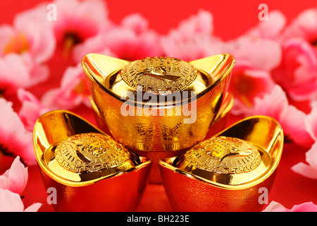 Vue avant de certains lingots d'or chinois entouré de cerisiers en fleurs sur fond rouge Banque D'Images