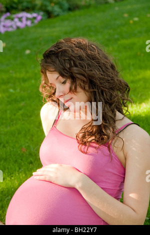 Femme enceinte assis sur l'herbe avec la main sur l'abdomen, Manitoba, Canada Banque D'Images