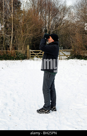 L'homme, habillé chaudement, l'observation des oiseaux dans la neige, Gillespie Park la réserve naturelle locale, Highbury London England UK Banque D'Images