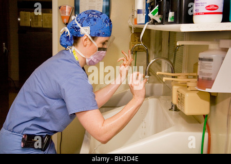 Vêtus de 'scrubs' et porter un masque chirurgical, une femme chirurgien se lave les mains soigneusement avant d'effectuer une opération. Banque D'Images