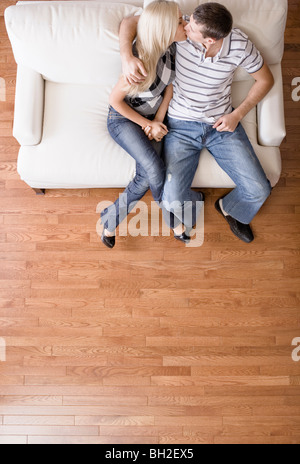 Jeune couple assis sur un siège d'amour, de couleur crème, et s'embrassant. Shot verticale Banque D'Images