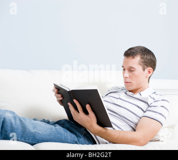 Portrait d'un homme de vous coucher sur un canapé avec un livre blanc. Format horizontal. Banque D'Images