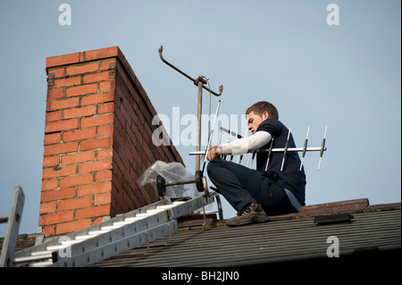 Un jeune ingénieur de la télévision l'installation d'un nouveau téléviseur numérique compatible sur antenne à une cheminée d'une maison Banque D'Images