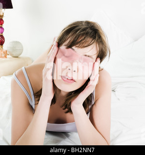 Femme allongée sur un lit blanc portant un masque de beauté du visage cryogéniques Banque D'Images