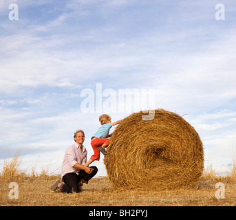 Man helping boy à grimper hay bale Banque D'Images