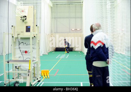 L'entraîneur de cricket de Sussex en utilisant Merlyn par BOLA bowling spin machine dans la pratique à l'école à l'intérieur de filets Banque D'Images