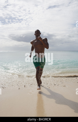 Jeune homme d'exécution de l'extérieur de la mer sur une plage déserte tropicale Banque D'Images