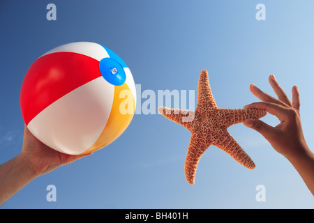 Un homme et une femme est main tenant un ballon de plage gonflable et une étoile de mer dans l'air contre un ciel d'été sans nuages, Bleu Banque D'Images