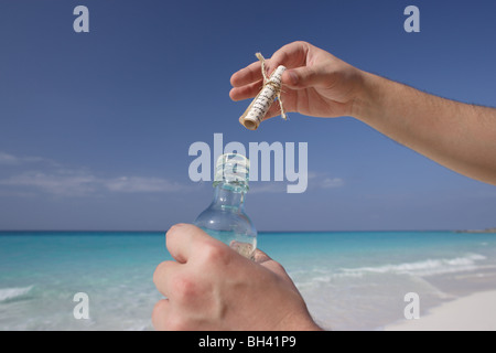 A man's hands holding un message dans une bouteille sur une plage tropicale déserte Banque D'Images