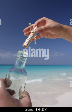A man's hands holding un message dans une bouteille sur une plage tropicale déserte Banque D'Images