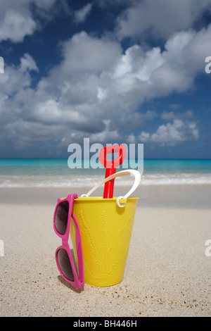 Un godet jaune, spade et une paire de lunettes de soleil sur une plage tropicale déserte Banque D'Images