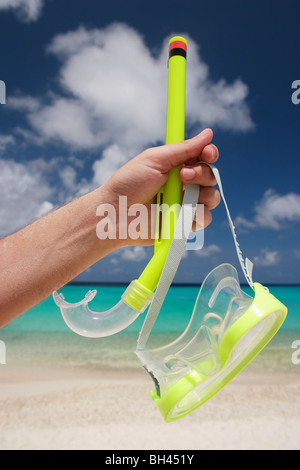 La main d'un homme tenant un masque et tuba jaune dans l'air sur une plage tropicale déserte Banque D'Images