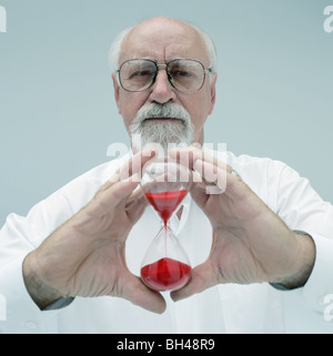 A senior man holding a glass sablier avec une expression grave Banque D'Images