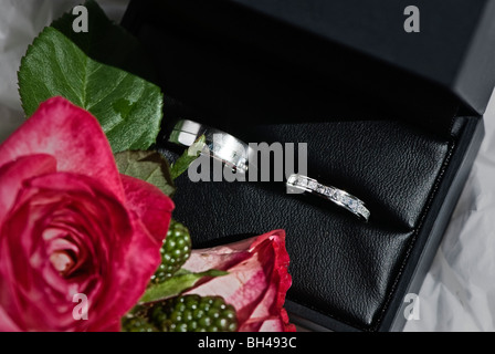 Les anneaux de mariage dans un coffret en cuir noir avec des fleurs en premier plan Banque D'Images