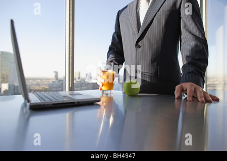 Un homme tenant un verre de jus d'orange à côté d'une pomme et d'un ordinateur portable sur un bureau bureau Banque D'Images