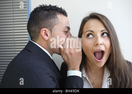 Un employé de bureau chuchoter dans l'oreille d'un collègue, avec une expression choquée Banque D'Images