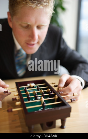 Un businessman playing miniature baby-foot at office desk,smiling Banque D'Images
