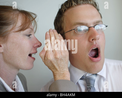 Un employé de bureau chuchoter dans l'oreille d'un collègue, avec une expression choquée Banque D'Images
