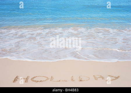 Le mot 'vacances' écrit dans le sable sur une plage tropicale Banque D'Images