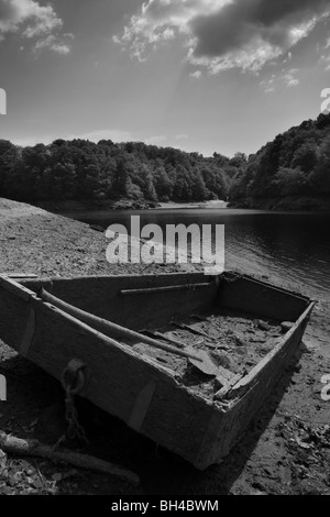 Composition en noir et blanc d'un vieux bateau à fond plat tiré vers le haut dans la boue à côté d'un grand fleuve. Banque D'Images