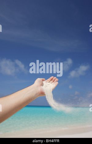 La main d'un homme versant le sable pris dans la brise sur une plage tropicale déserte Banque D'Images