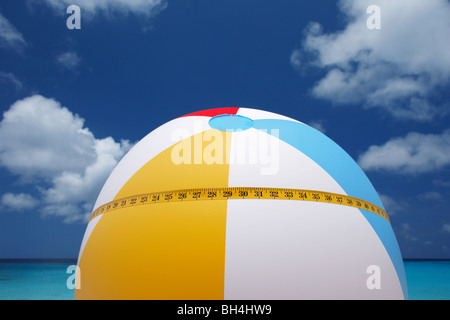 Un ruban de mesure enroulée autour d'un ballon de plage gonflable aux couleurs vives à l'encontre d'une mer bleue et le ciel tropical Banque D'Images