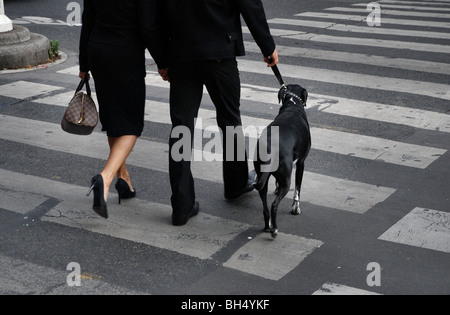 Paris : un couple vêtu de noir sur un passage clouté avec un chien noir Banque D'Images