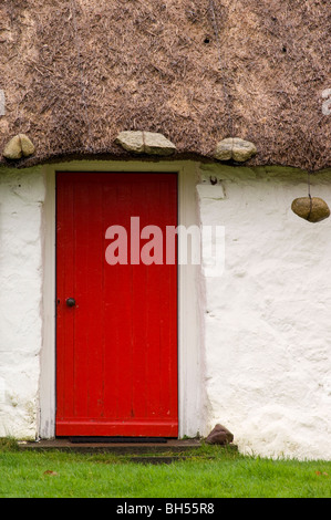 Chaume traditionnel chalet au crofting Luib, île de Skye, porte rouge. Banque D'Images