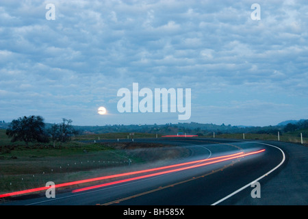 California Highway 132 dans la nuit avec la Lune se levant et des projecteurs et feux arrière des stries claires Banque D'Images